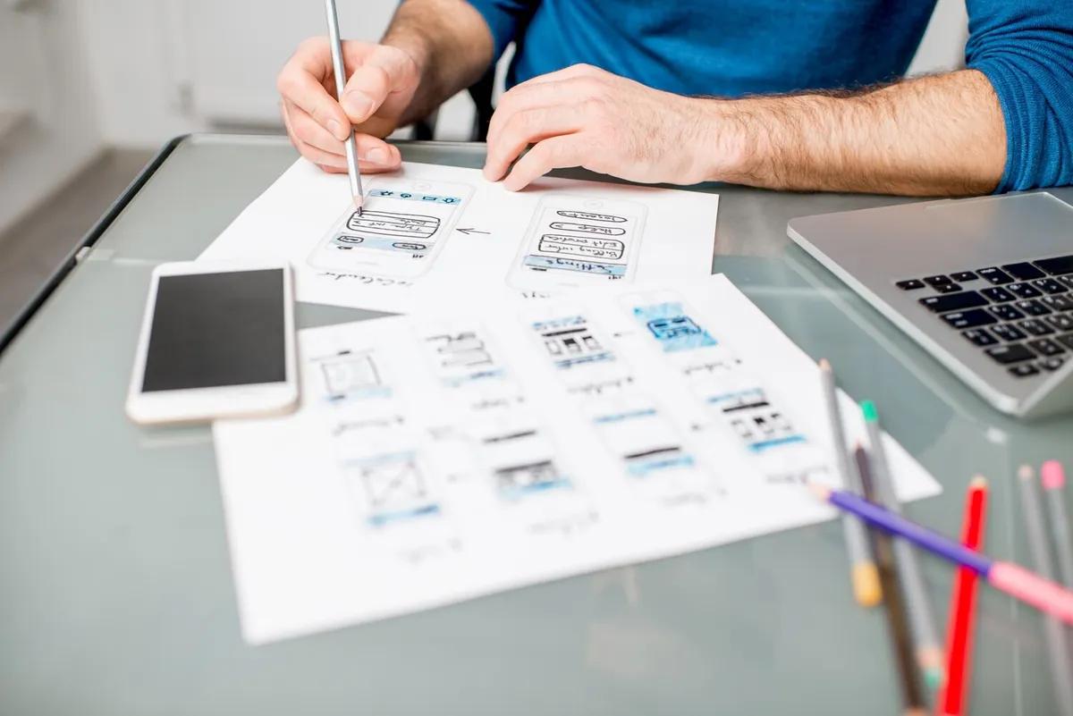 Un designer dessine au crayon des écrans d'application mobile sur une feuille de papier