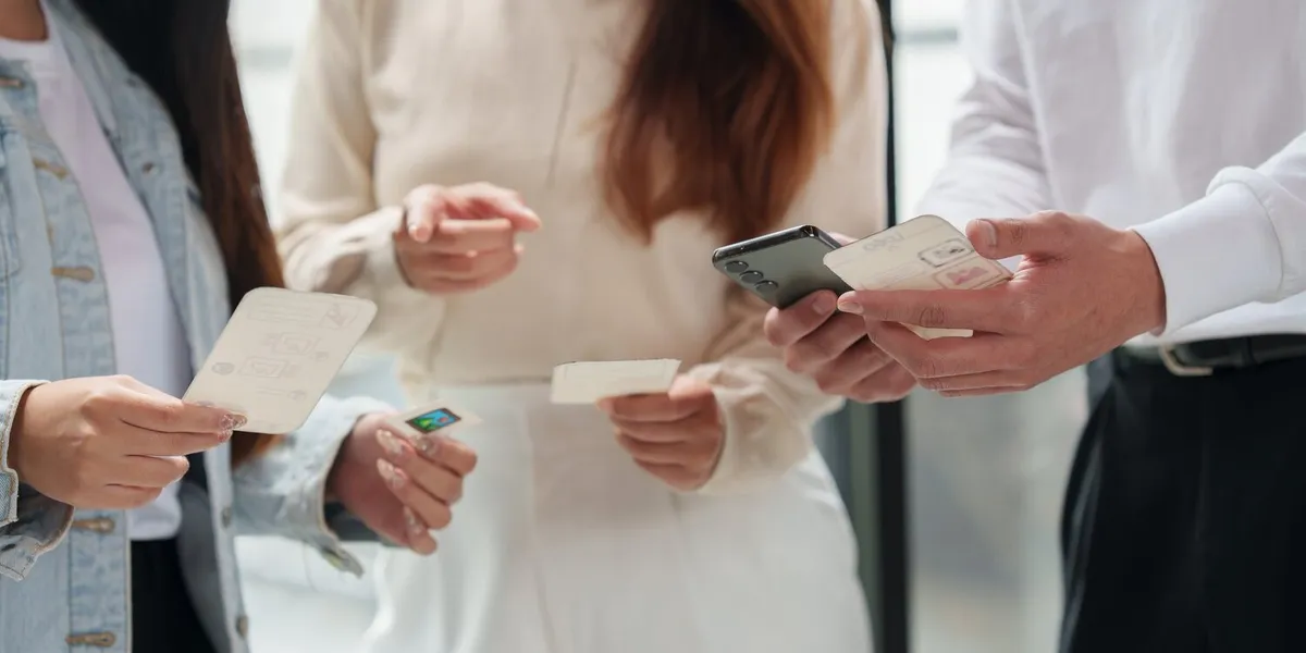 Des mains tiennent des cartes de prototype papier à côté d'un smartphone, pour tester un parcours